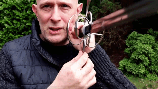 a man in a black vest holds a sword in his hands