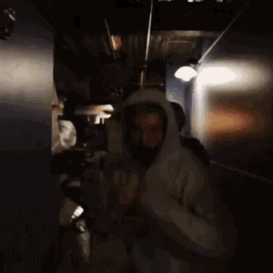 a man in a white hoodie is standing in a dark room