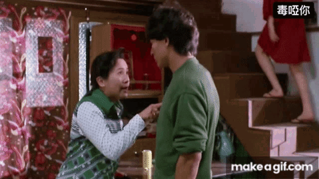 a man and a woman are standing next to each other in a room with a woman walking down the stairs behind them