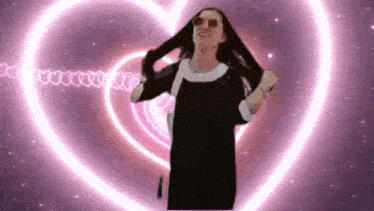 a woman wearing sunglasses is standing in front of a pink heart shaped tunnel .