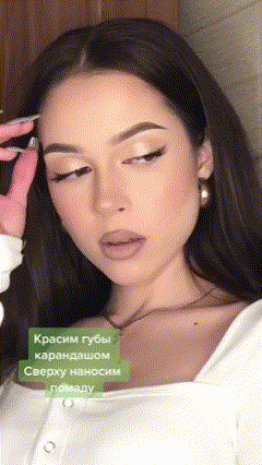 a woman wearing a white shirt and earrings is applying makeup