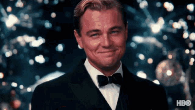 a man in a tuxedo is smiling in front of a blurred background with hbo written on the bottom