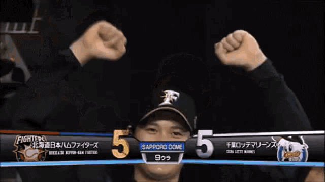 a man wearing a sapporo dome hat holds his fists up in the air