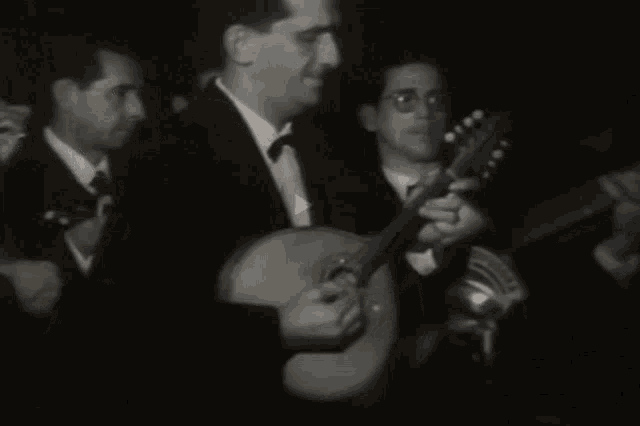a man in a tuxedo is playing a guitar in a dark room