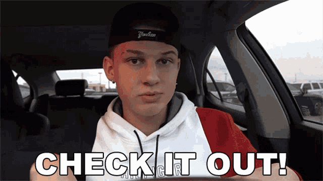 a young man in a yankees hat is sitting in a car with the words check it out below him