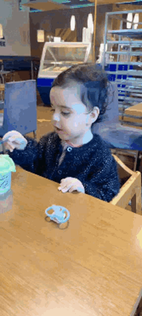 a little girl with a pacifier sits at a table