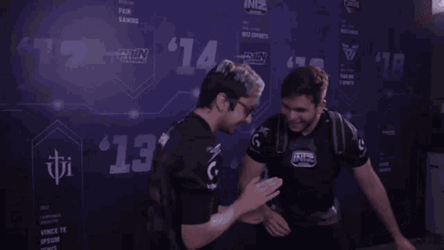 two men are shaking hands in front of a wall with logos on it .