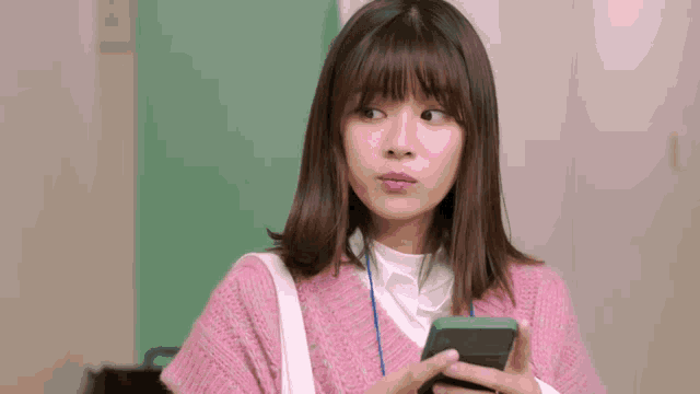 a woman in a pink sweater is holding a cellphone