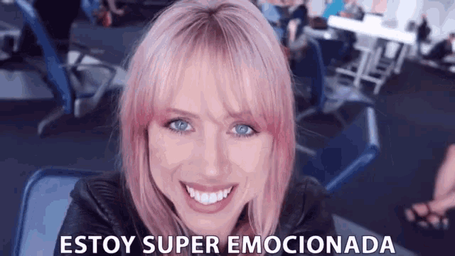 a woman with pink hair and blue eyes is smiling and the words estoy super emocionada are above her