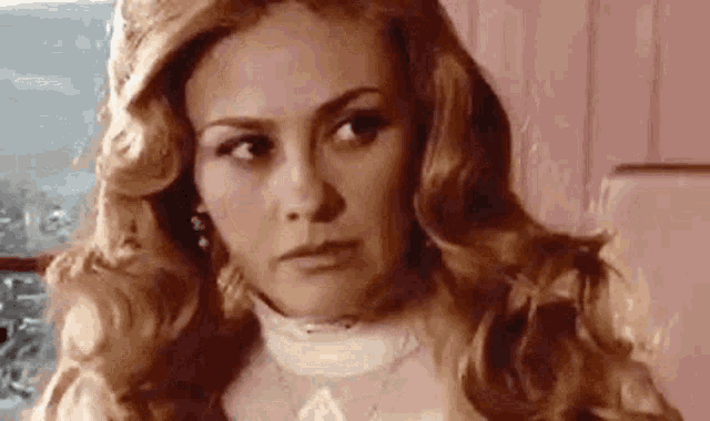 a close up of a woman with long blonde hair wearing a white sweater and necklace .