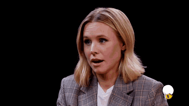 a woman wearing a plaid jacket and a white shirt has her mouth open