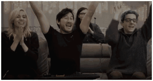 a group of people are sitting on a couch raising their arms in the air .