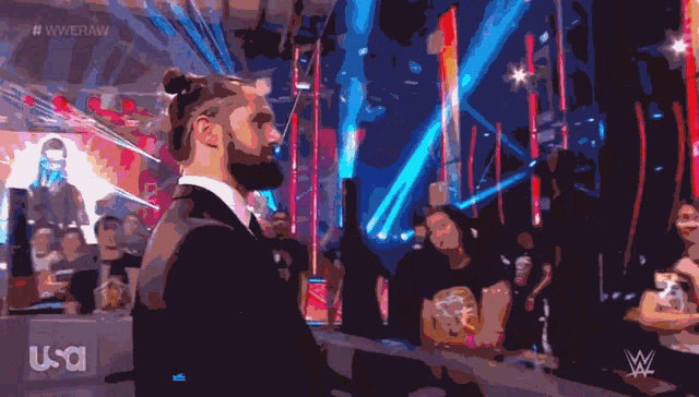a man in a suit stands in front of a crowd at a wrestling show