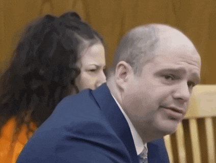 a bald man in a suit and tie is sitting next to a woman in a jail cell .