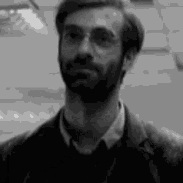 a black and white photo of a man with a beard and glasses .