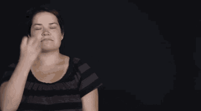 a woman in a striped shirt is making a funny face with her hand .