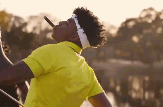a man wearing a yellow shirt and a headband is smoking a cigar