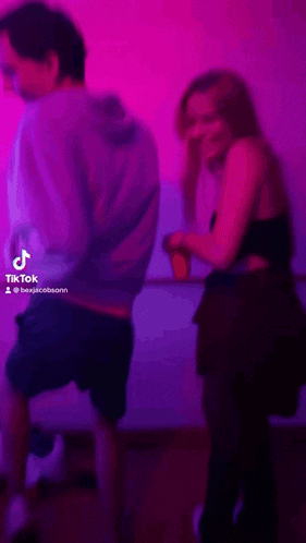 a man and a woman are dancing in front of a pink wall with tiktok written in the corner