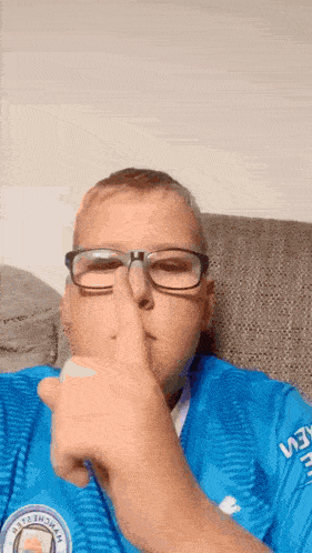 a boy wearing glasses and a blue shirt is making a shhh sign