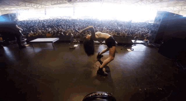 a woman is doing a handstand on a stage in front of a large crowd