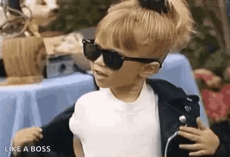 a little girl wearing sunglasses and a leather jacket is dancing .