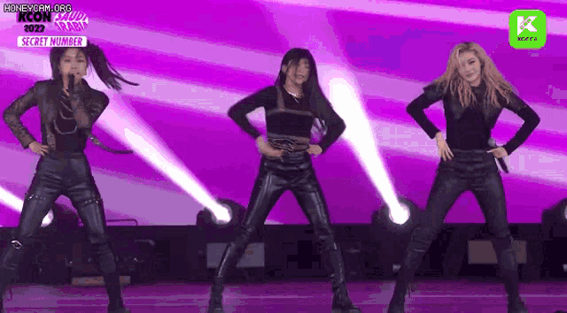 a group of women are dancing on a stage with purple lights behind them .