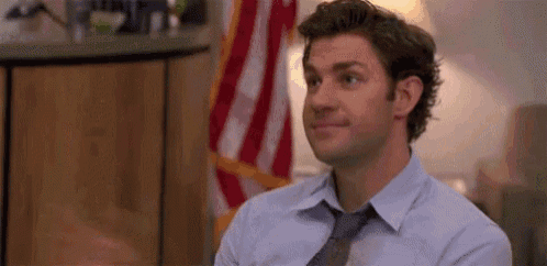 a man in a tie is sitting in front of an american flag .