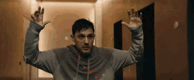 a man in a grey hoodie is standing in a hallway with his hands up