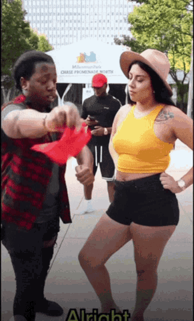 a woman in a yellow tank top is standing in front of a man in a red hat