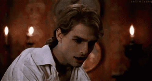 a man in a white shirt with blood on his face is standing in front of candles .