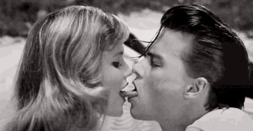 a black and white photo of a man and woman kissing on the beach .