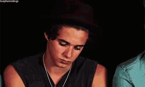 a young man with curly hair is wearing a black tank top and a necklace around his neck .