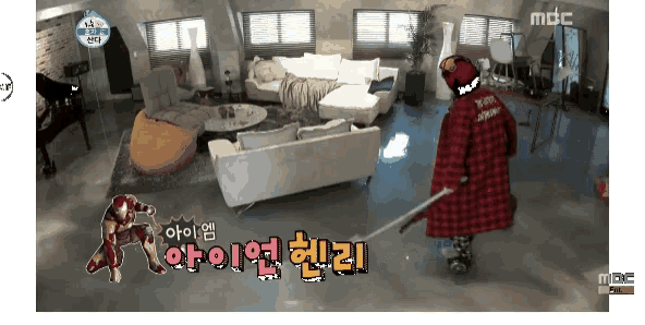 a man in a red plaid coat is holding a sword in a living room with a mbc logo behind him