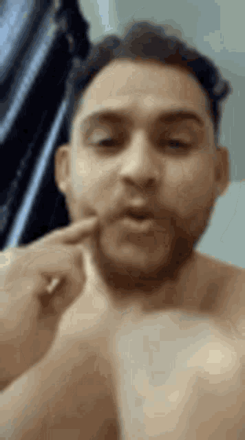 a shirtless man with a beard is scratching his face with his finger .