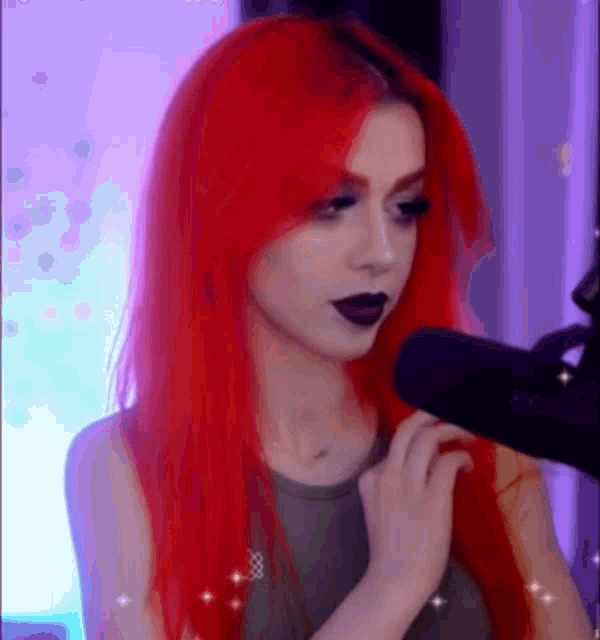 a woman with red hair is standing in front of a microphone and looking at the camera .
