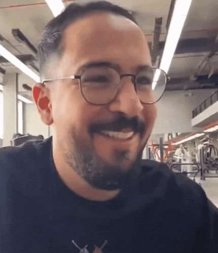 a man wearing glasses and a black shirt smiles in a gym