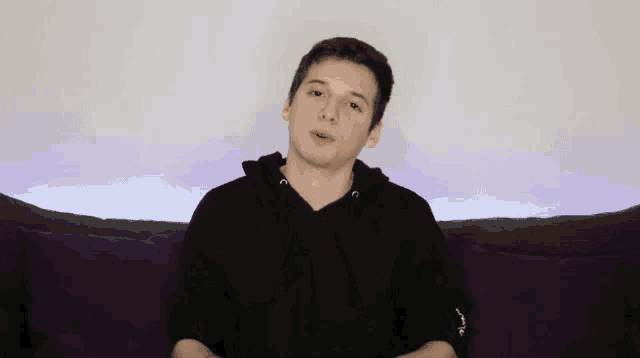 a young man is sitting on a couch wearing a black hoodie