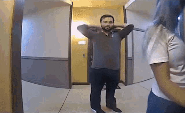 a man is standing in a hallway with his hands behind his head and a woman is standing behind him