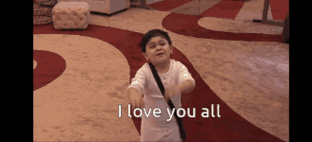 a little boy is standing on a red and white rug with the words i love you all above him