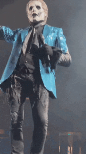 a man in a blue jacket and black pants is holding a microphone on a stage .