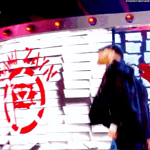 a man is standing in front of a brick wall with a red circle on it
