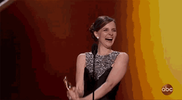 a woman in a black dress is laughing while holding a trophy .