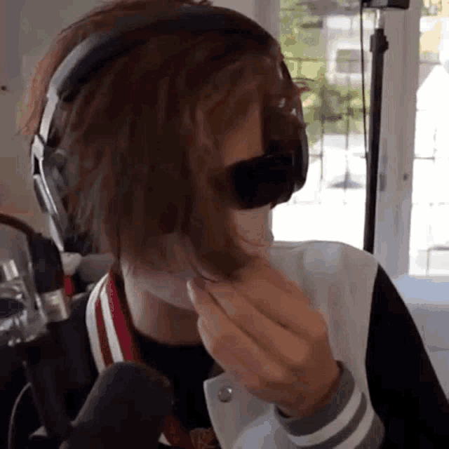 a person wearing headphones and a baseball jacket is holding their hair .