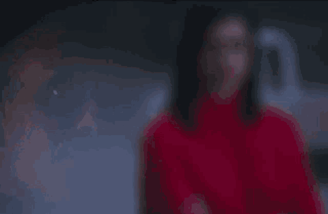 a woman in a red turtleneck sweater is standing with her arms crossed and looking at the camera .
