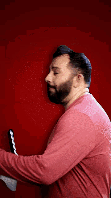a man with a beard wearing a red shirt is holding a laptop