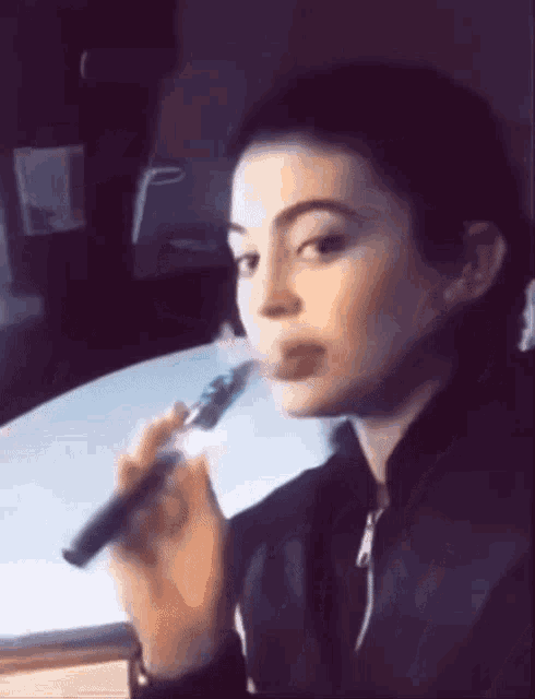 a woman is smoking an electronic cigarette while sitting at a desk .