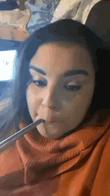 a woman in an orange sweater is smoking a hookah .