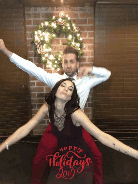 a man is carrying a woman on his shoulders in front of a christmas wreath that says happy holidays 2019