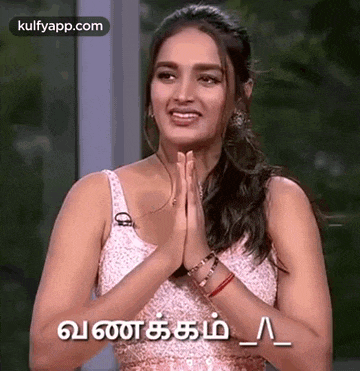 a woman in a pink dress is smiling and holding her hands together .