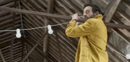 a man in a yellow jacket is hanging a string of lights from the ceiling of a building .